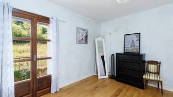 Ein Zimmer mit Holzboden, einem schwarzen Kommoden, einem Stuhl, einem Heizkörper und einem Fenster mit Vorhängen.