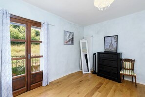Una habitación con piso de madera, un aparador negro, una silla, un radiador y una ventana con cortinas.