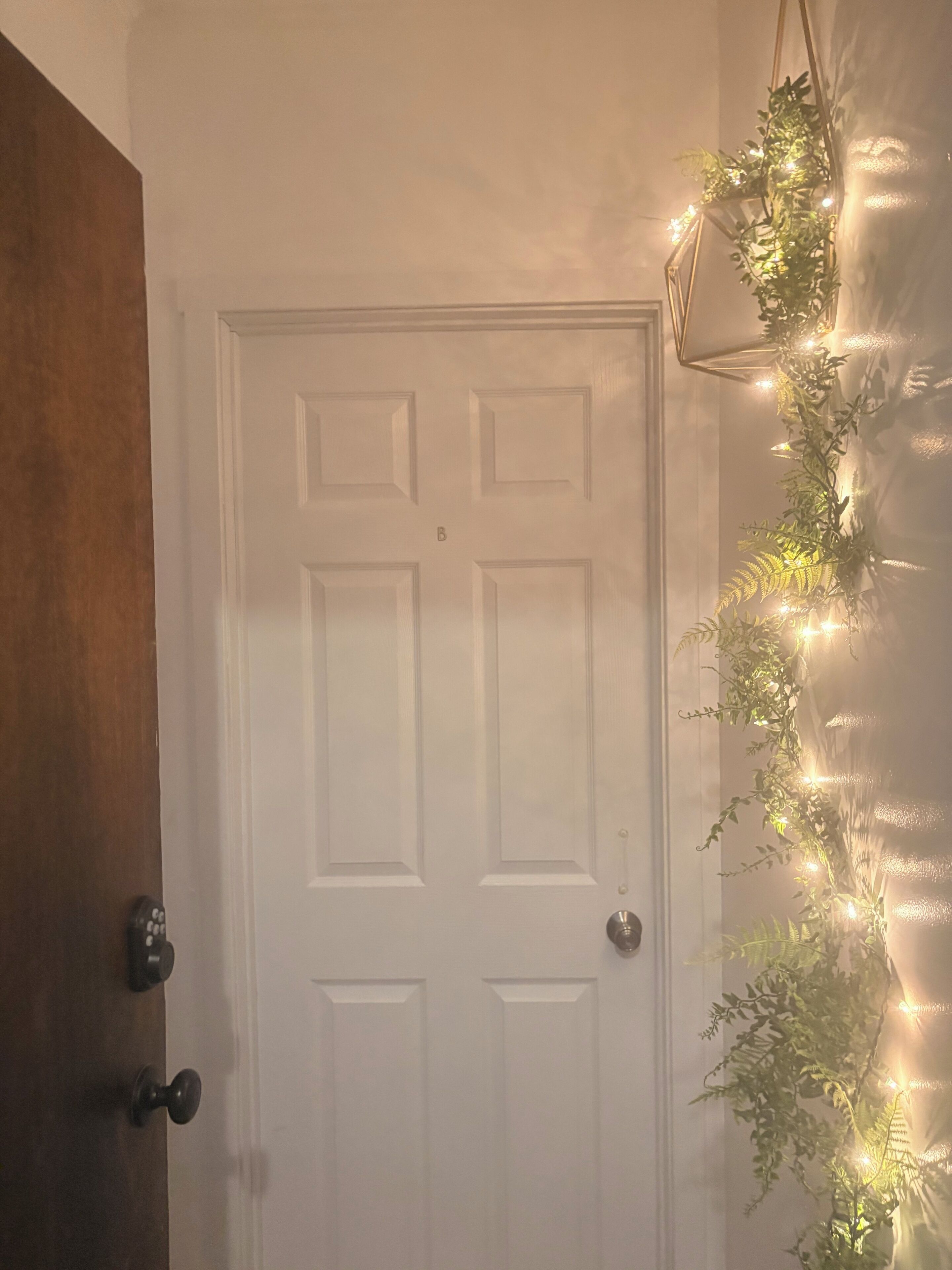 A white door with a keyhole and a doorknob, a wooden door frame to the left, and a string of lights on the wall to the right.