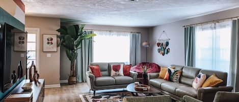 Un salon comprenant un canapé, une table basse, un téléviseur et une grande plante.