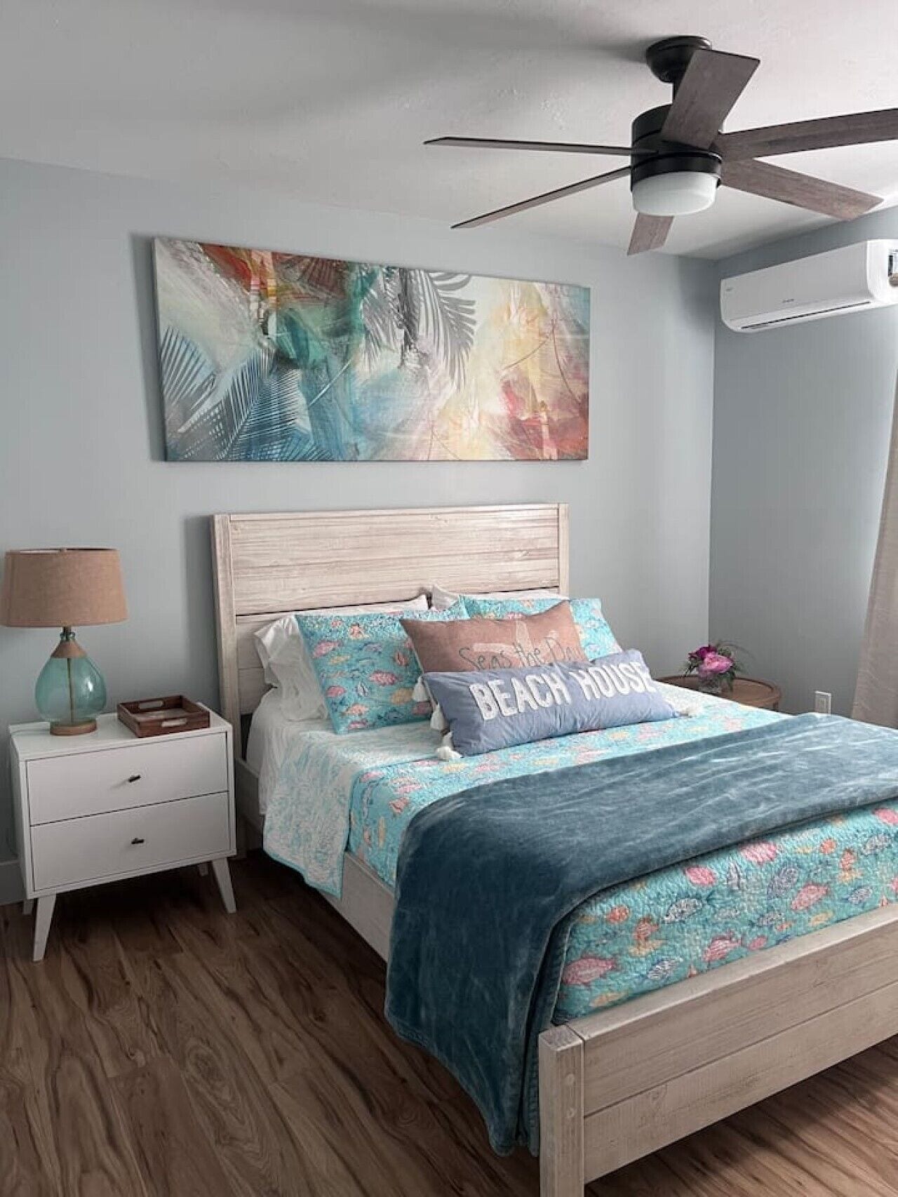 A bedroom with a bed, a nightstand, a lamp, a ceiling fan, and a wall-mounted air conditioner.