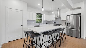 A modern kitchen with white cabinetry, a stainless steel refrigerator, and bar stools. - Mountain Escape - Minutes to Snowbasin & Pineview - Sleeps 8 (Mountain Green)