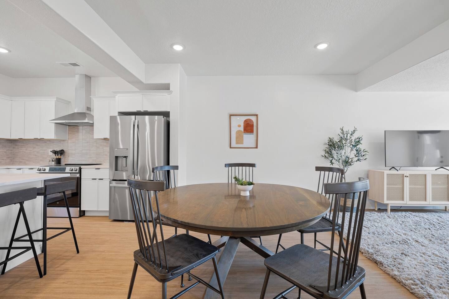 A modern kitchen with white cabinetry, a round wooden dining table, and four chairs.