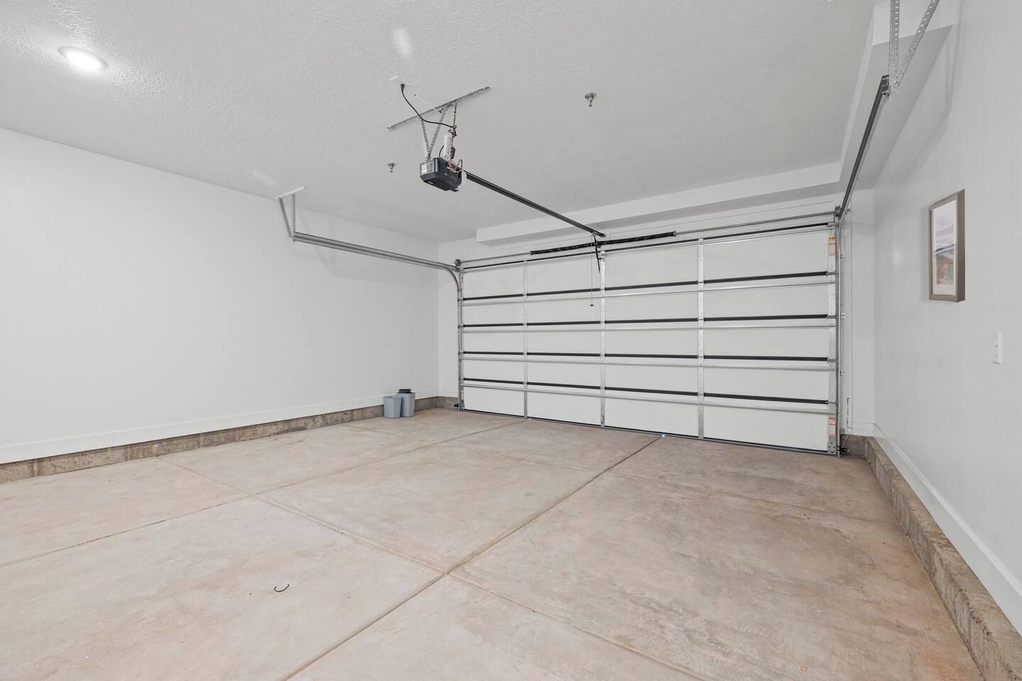 A clean, empty garage with a white door and a ceiling-mounted projector.