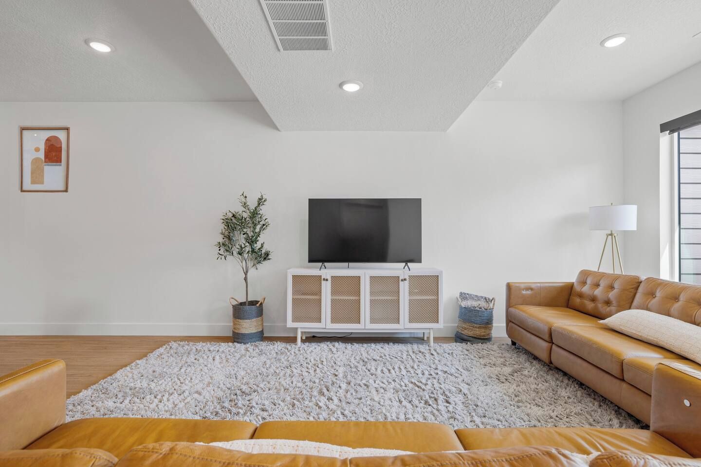 Una sala de estar moderna con un televisor de pantalla plana grande, un mueble blanco, un sofá de cuero marrón y un tapete blanco y esponjoso.