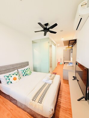 Quarto de hotel com uma cama, ventoinha no teto, televisão e escrivaninha.