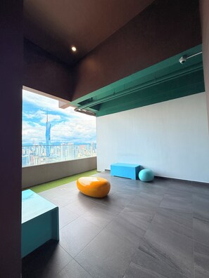 Interior moderno com vista para o horizonte urbano, uma parede verde e uma área de estar com uma poltrona laranja arredondada e um banco azul.