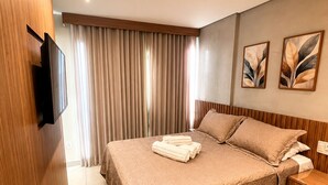 A hotel room with a bed, a TV mounted on the wall, a bedside table, and a curtain. - Apartment with furnished balcony | Gym | Swimming pool | Complete linens (Goiânia)