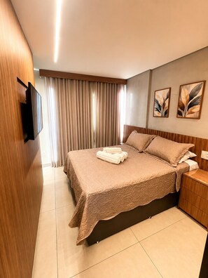 Ein Hotelzimmer mit Bett, Wandfernseher, Nachttisch und Vorhang.