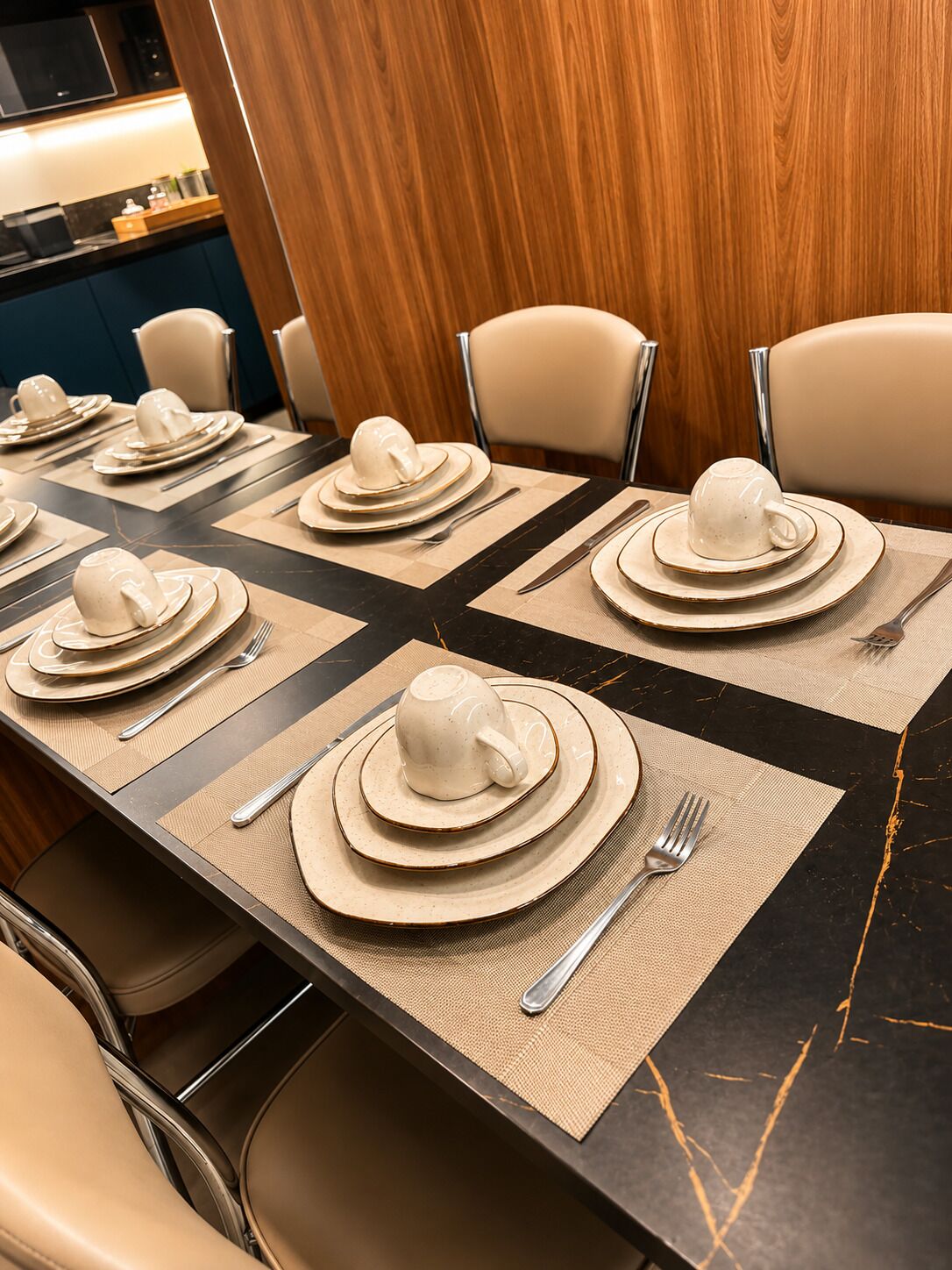 A dining table set with plates, bowls, and cutlery, with a wooden panel and chairs in the background.
