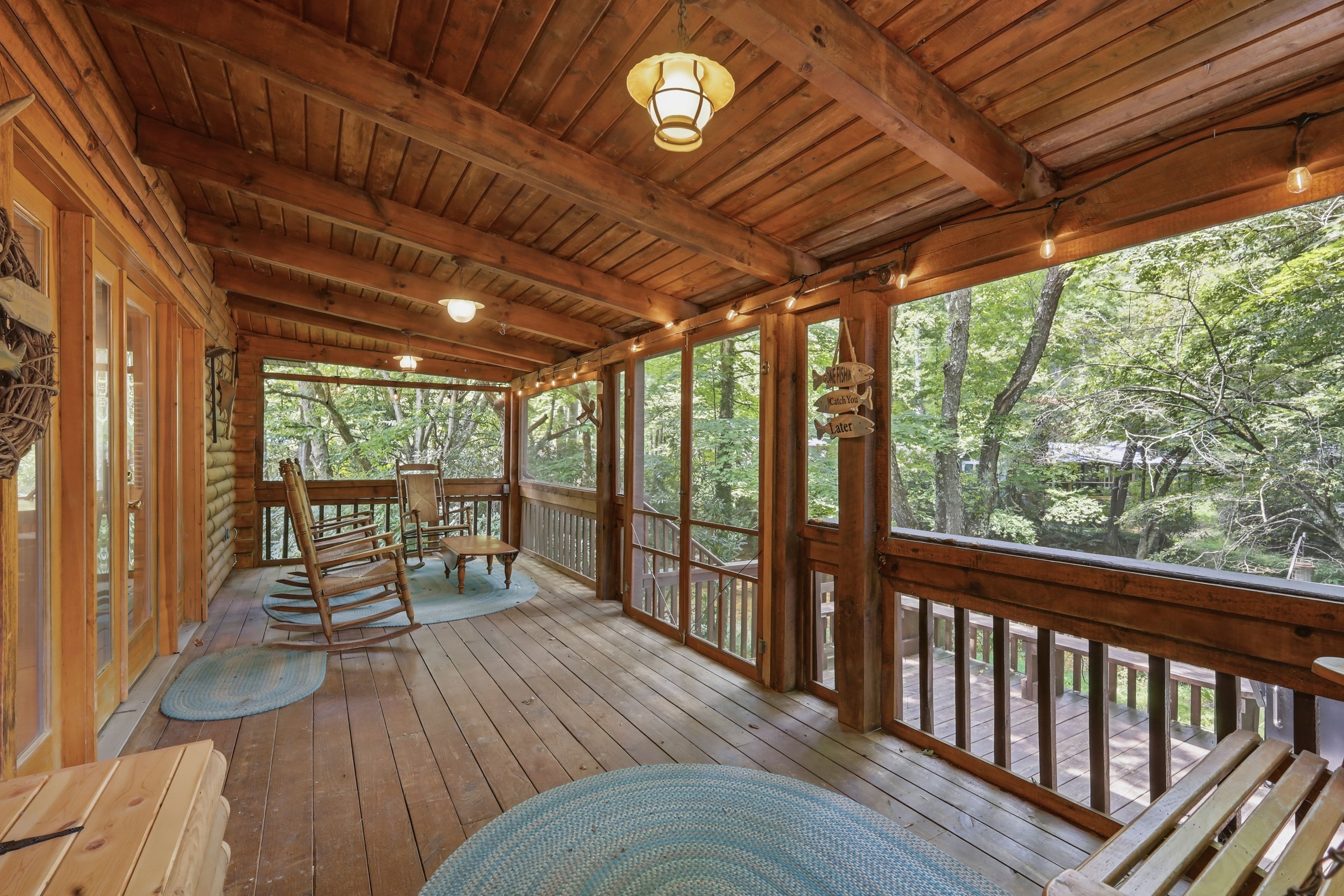 A wooden deck with a rocking chair and a table, surrounded by large windows offering a view of the forest.