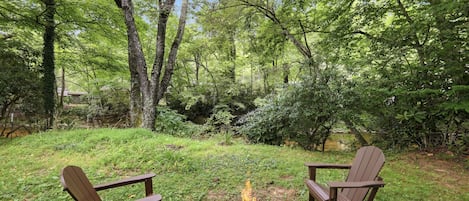 A backyard with a fire pit and two Adirondack chairs.