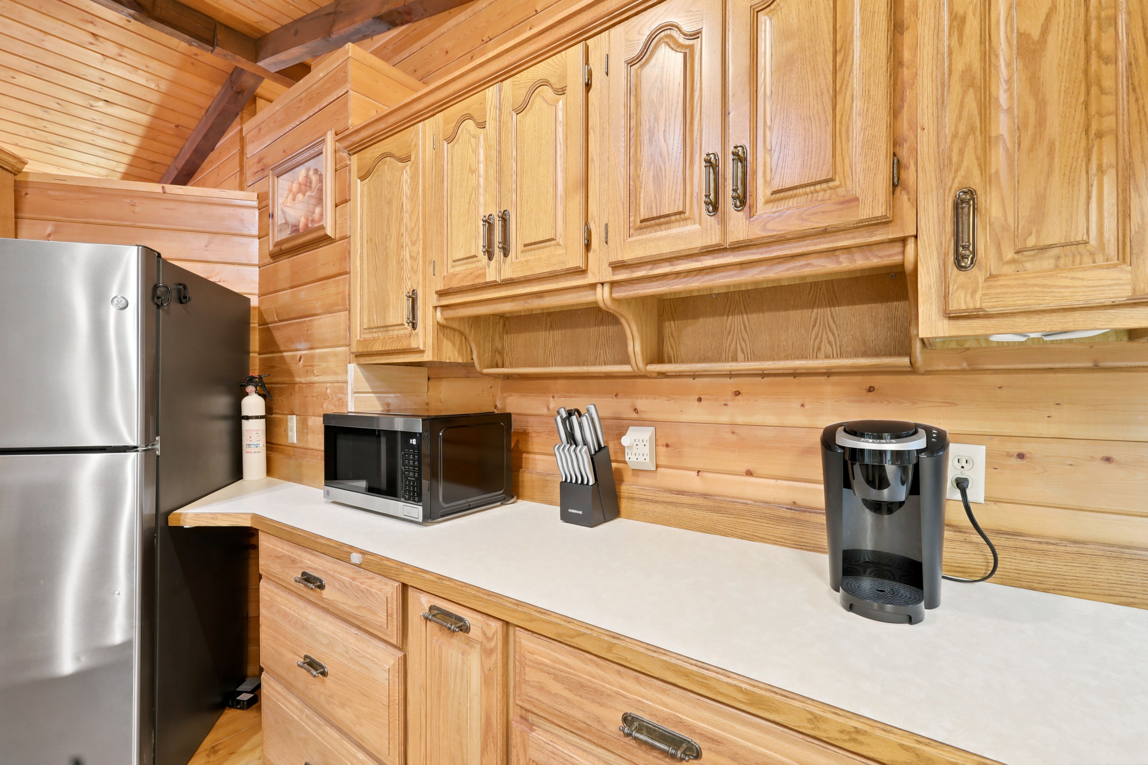A kitchen with wooden cabinets, a stainless steel refrigerator, a microwave, and a coffee machine.