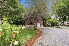 A log cabin with a stone foundation, surrounded by a gravel driveway and a garden with various plants and flowers. - Apples and Antlers - Quaint Riverside Log Cabin in Linville Harbor (Newland)