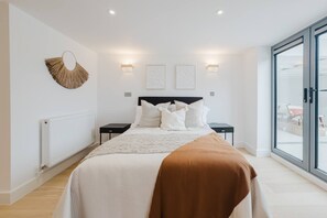 Een moderne slaapkamer met een groot bed, nachtkastjes, een radiator en uitzicht door een glazen deur.