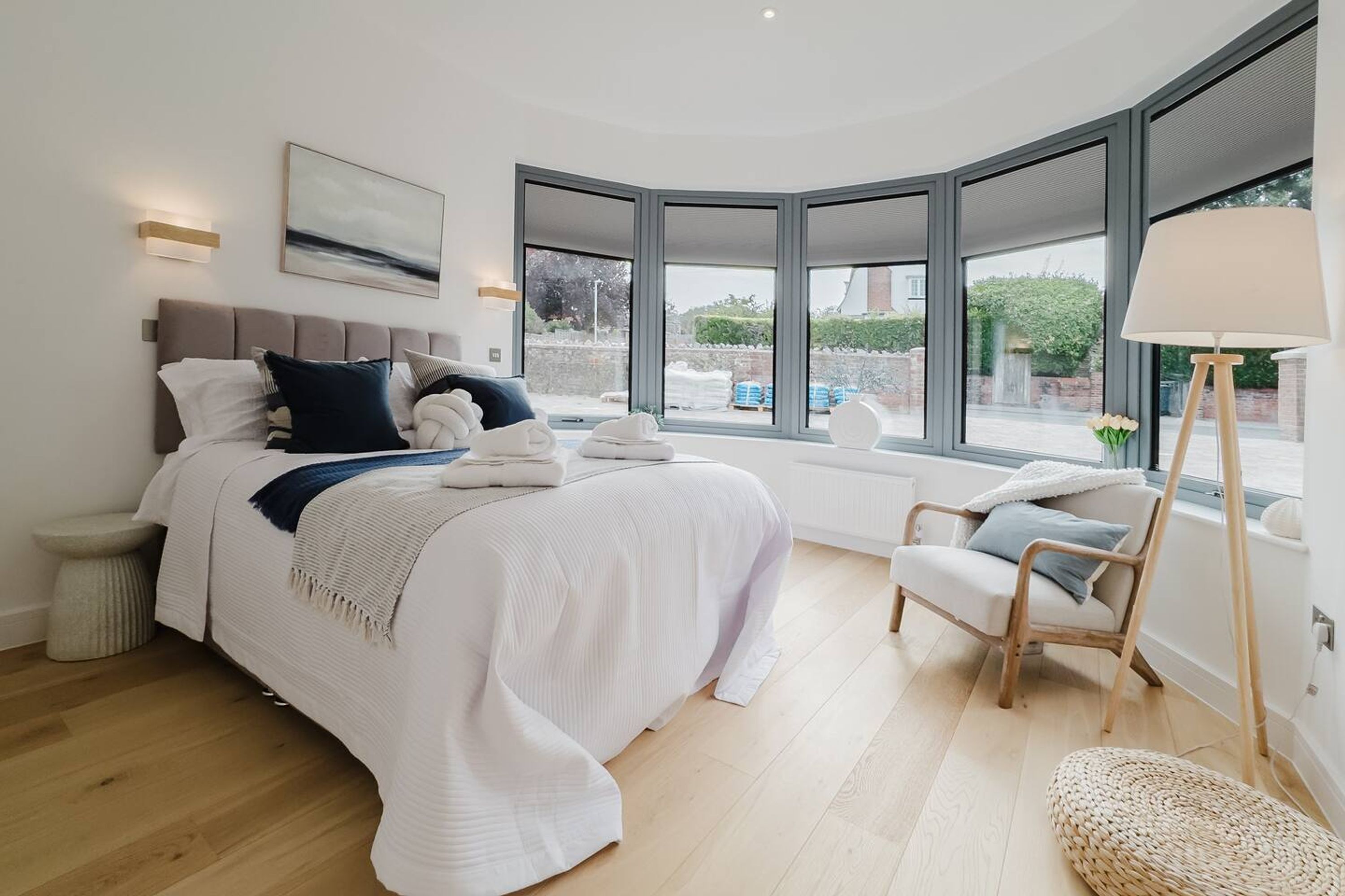 Une chambre à coucher moderne avec une fenêtre incurvée, un lit recouvert de draps blancs, une table de chevet et une chaise.