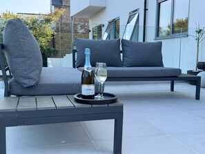 Een moderne zithoek buiten met een bank en een tafel, een fles champagne, en een glas op tafel.