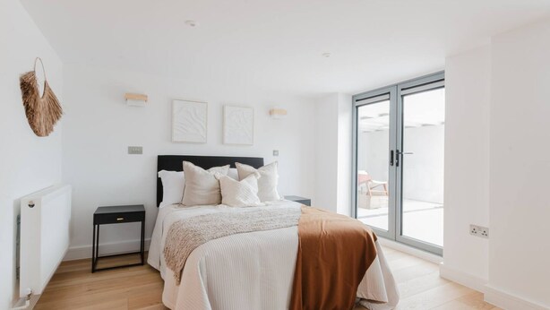 A modern bedroom with a bed, bedside tables, a radiator, and a large window. - Broadstairs Duplex With Terrace Near Stone Bay FT1 (Broadstairs)