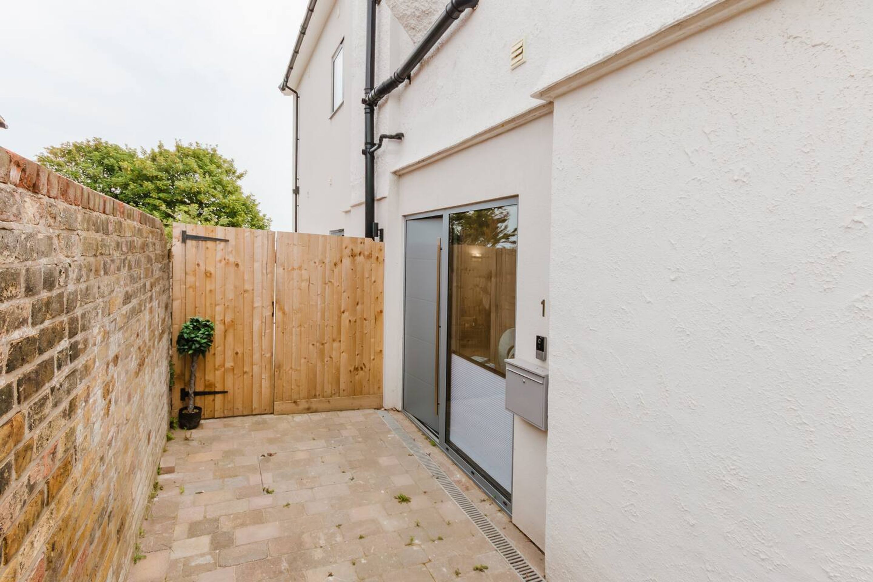 A narrow courtyard with a brick wall, a wooden fence, and a door leading to a garage.