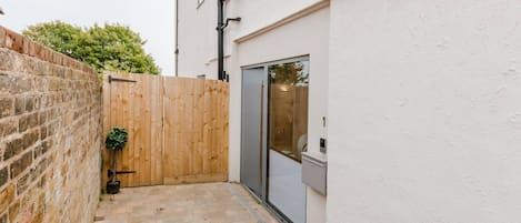 A narrow courtyard with a brick wall, a wooden fence, and a door leading to a garage.