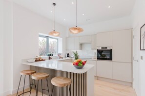 A modern kitchen with a central island, bar stools, a large window, and a hanging light fixture. - Broadstairs Duplex With Terrace Near Stone Bay FT1 (Broadstairs)