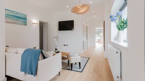 A modern living room with a sofa, a television, and a window with flowers. - Broadstairs Duplex With Terrace Near Stone Bay FT1 (Broadstairs)