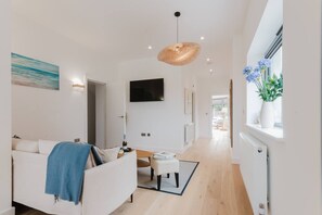 A modern living room with a sofa, a television, and a window with flowers. - Broadstairs Duplex With Terrace Near Stone Bay FT1 (Broadstairs)
