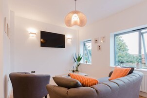 Una sala moderna con un sofá gris, dos sillones, un televisor de pantalla plana y un ventanal con vistas a la vegetación.