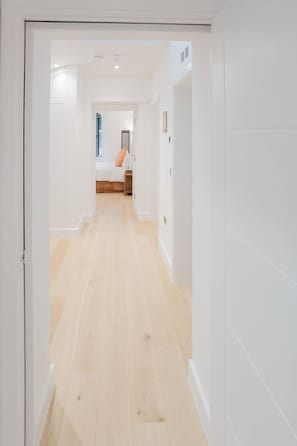 A hallway with a wooden floor leading to a bedroom with a bed and a nightstand. - Broadstairs 2 Bed Flat Balcony FT2 by Adliv (Broadstairs)