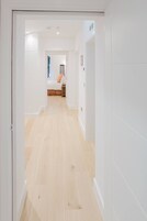 Um corredor com piso de madeira que leva a um quarto com cama e mesa de cabeceira.