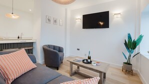 A modern living room with a sofa, armchair, coffee table, and a flat-screen TV mounted on the wall. - Broadstairs 2 Bed Flat Balcony FT2 by Adliv (Broadstairs)