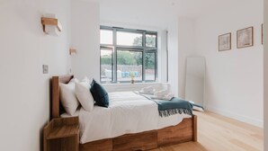 A bedroom with a wooden bed, white bedding, a window with a view, and a whiteboard on the wall. - Broadstairs 2 Bed Flat Balcony FT2 by Adliv (Broadstairs)