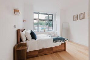 A bedroom with a wooden bed, white bedding, a window with a view, and a whiteboard on the wall. - Broadstairs 2 Bed Flat Balcony FT2 by Adliv (Broadstairs)