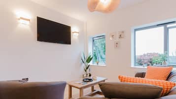 A modern living room with a flat-screen TV, a wooden coffee table, and a sofa with orange cushions.