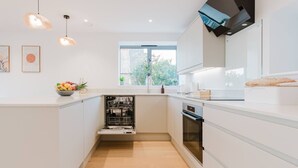Una cucina moderna con mobili bianchi, lavastoviglie, forno e una finestra che offre luce naturale.