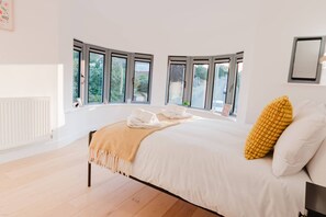 Une chambre avec un grand lit, de nombreuses fenêtres, un radiateur et un tableau encadré accroché au mur.