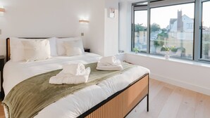 Un letto rifatto con lenzuola e asciugamani bianchi, una testiera in legno e un'ampia finestra con vista sulle case.