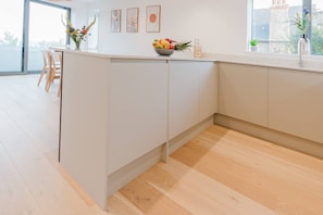 A modern kitchen with a white countertop, wooden flooring, and a large window providing natural light. - Seaview 2 Bed Retreat Balcony FT3 by Adliv (Broadstairs)
