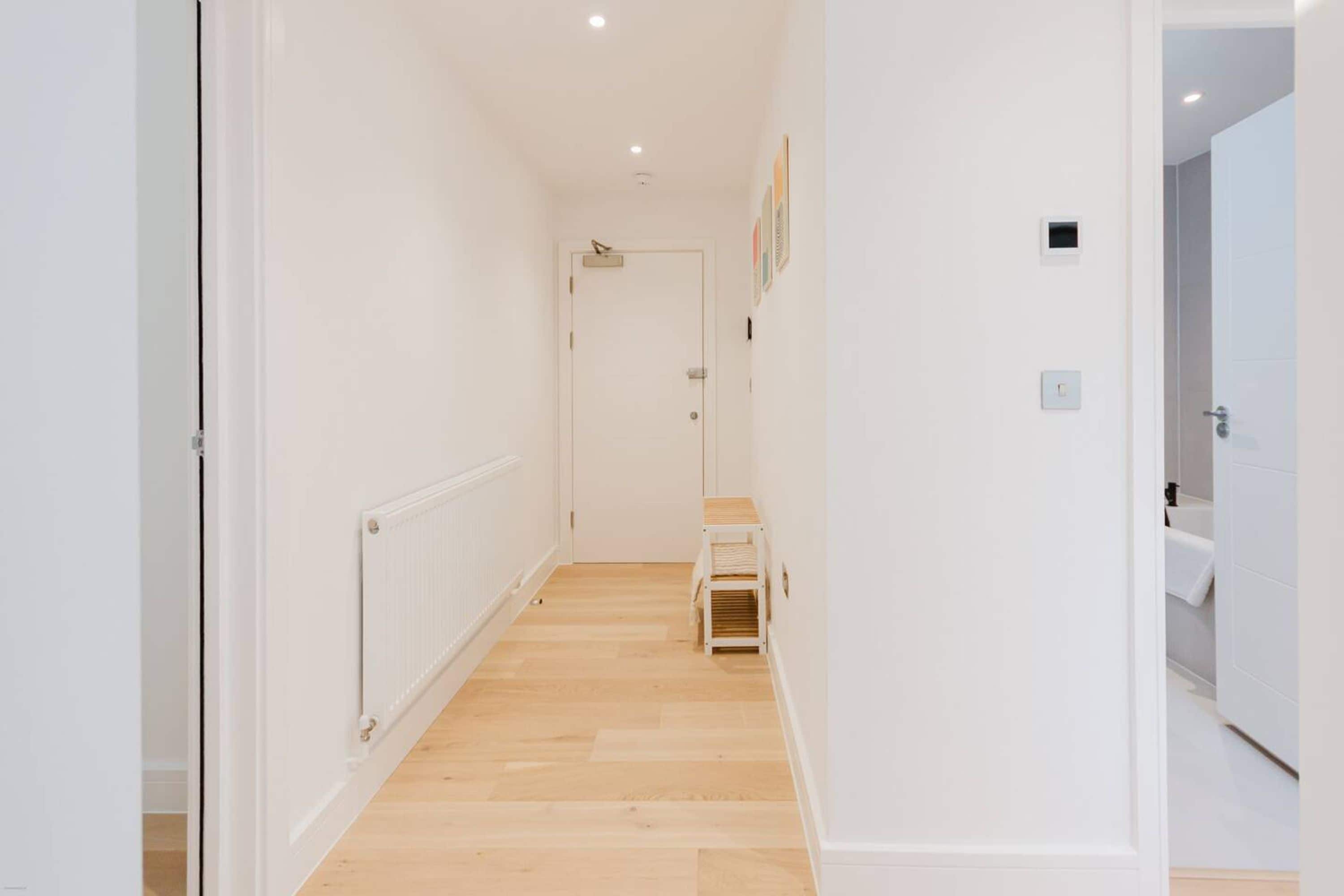 A hallway with a radiator, a door at the end, and a small shelf with folded items.