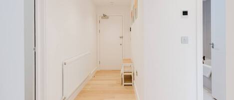 A hallway with a radiator, a door at the end, and a small shelf with folded items.