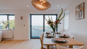Un'area pranzo con un tavolo apparecchiato per quattro persone, un vaso con fiori e vista mare attraverso un'ampia finestra.