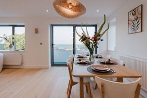 Ein Essbereich mit einem Tisch für vier Personen, einer Blumenvase und Meerblick durch ein großes Fenster.