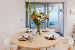 Ein Essbereich mit einem runden Tisch, gedeckt für vier Personen, einer Vase mit Blumen und Blick durch eine Glastür.