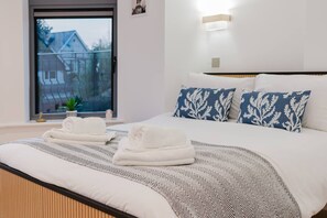 A bedroom with a bed, pillows, a window, and a view of a house. - Broadstairs Sea-view 2-balcony Flat FT4 by Adliv (Broadstairs)