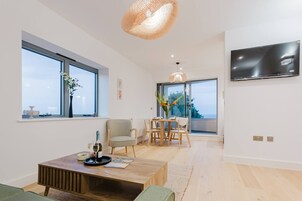 Uma sala de estar moderna com área de jantar, grandes janelas, televisão de tela plana e uma mesa de centro de madeira.