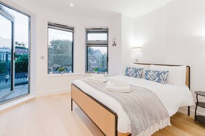 Ein modernes Schlafzimmer mit einem großen Bett, zwei Fenstern und Blick ins Freie.