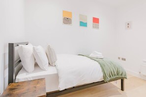Ein Einzelbett mit weißer Bettwäsche, Kissen und einer grünen Tagesdecke, sowie ein Holz-Kopfteil.