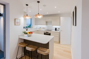 A modern kitchen with a central island, bar stools, pendant lighting, and a view through the window. - Broadstairs Sea-view 2-balcony Flat FT4 by Adliv (Broadstairs)