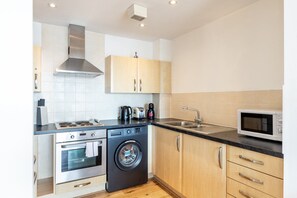 A compact kitchen with a washing machine, a microwave, a stove, and a sink. - Bright Stepney Green City Stay (London)