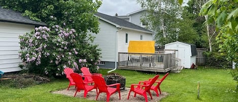 A backyard with a deck, red chairs, and a small shed.